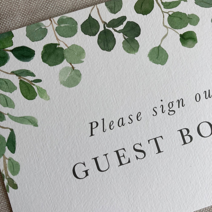 Guest book sign with green leaf design and text on a textured surface