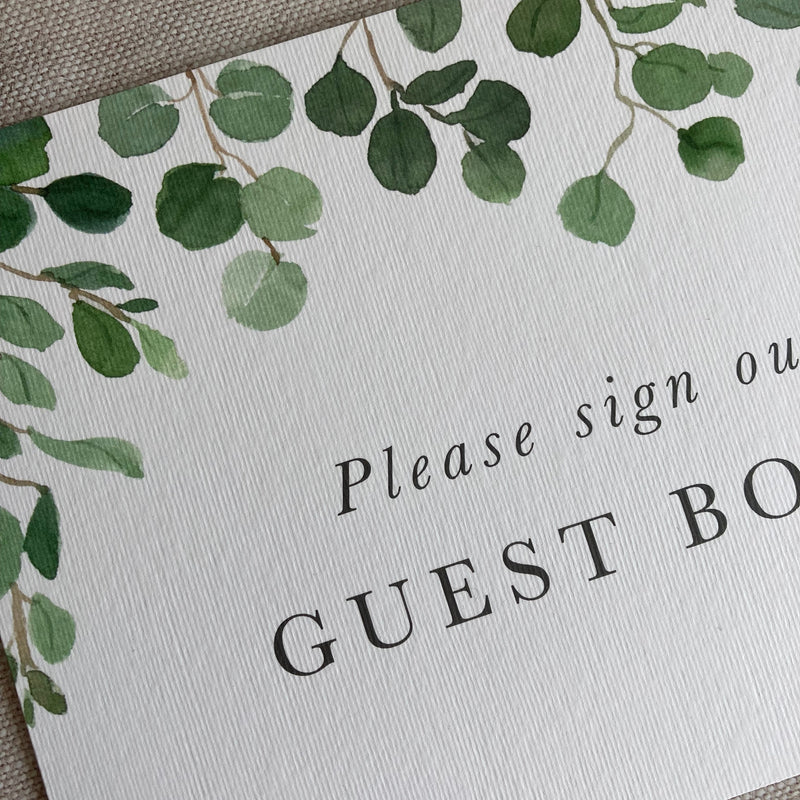Guest book sign with green leaf design and text on a textured surface